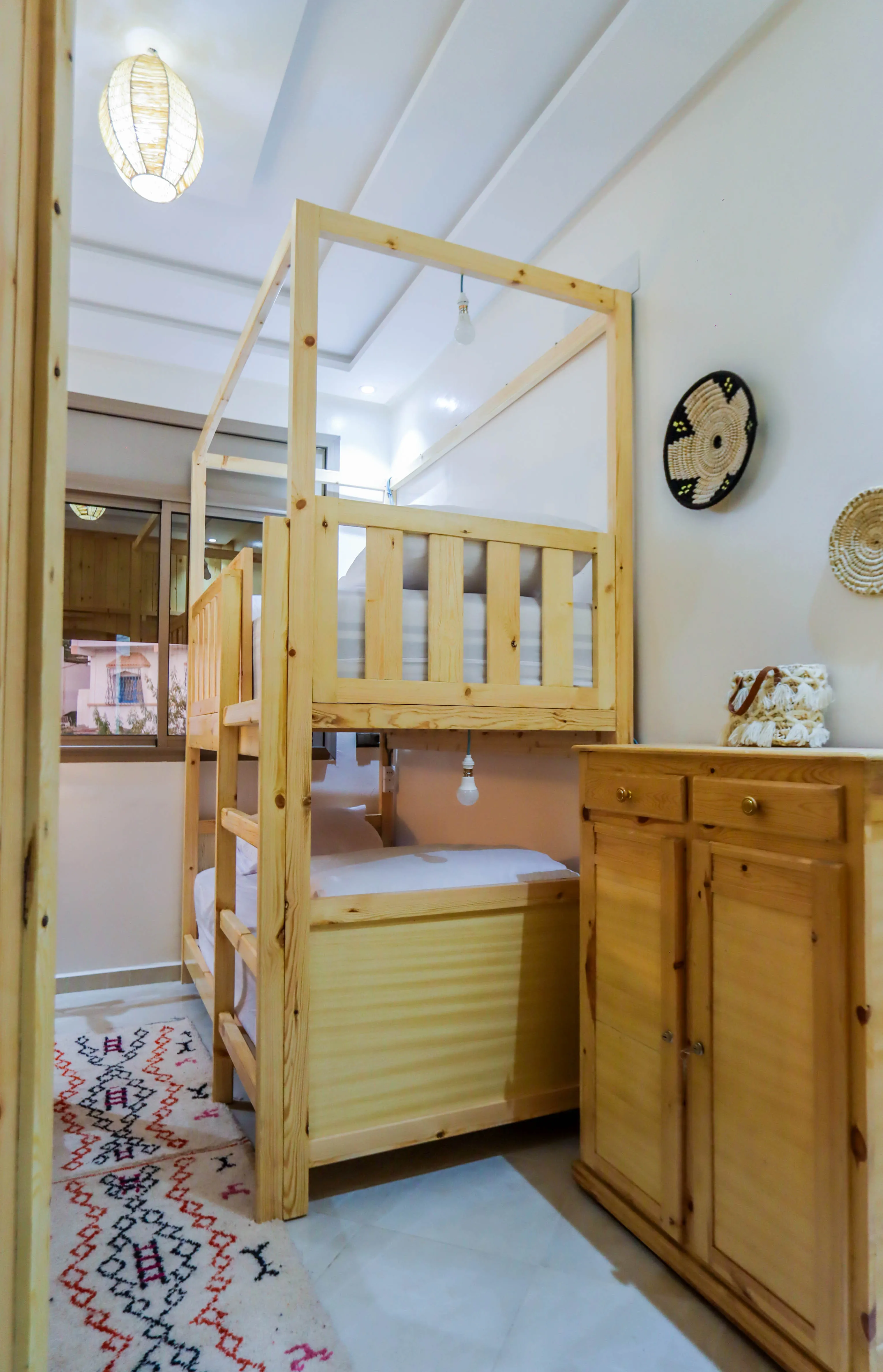 Small bedroom with wooden bunk beds, patterned rug, wooden cabinet, and decorative wall plates.