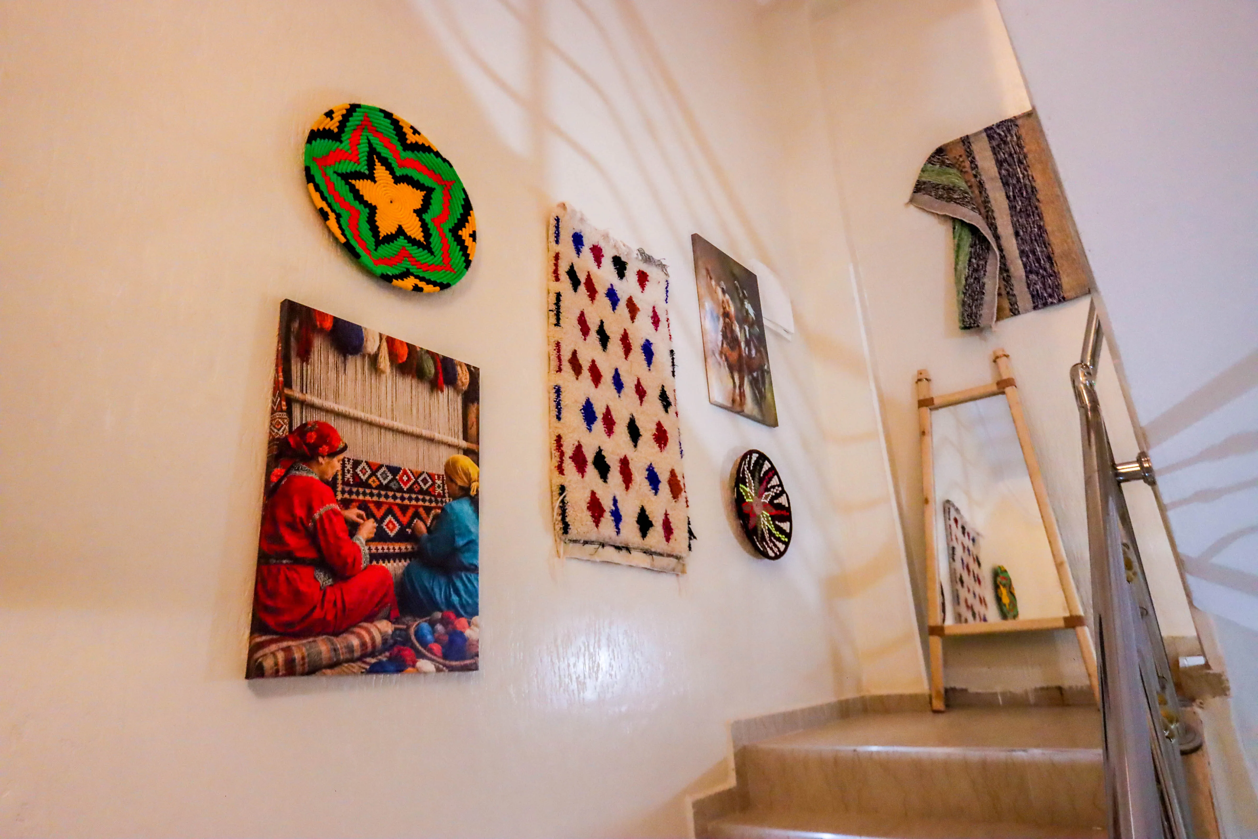 Staircase wall decorated with colorful woven baskets, a textile, and pictures of women weaving and a horse rider.