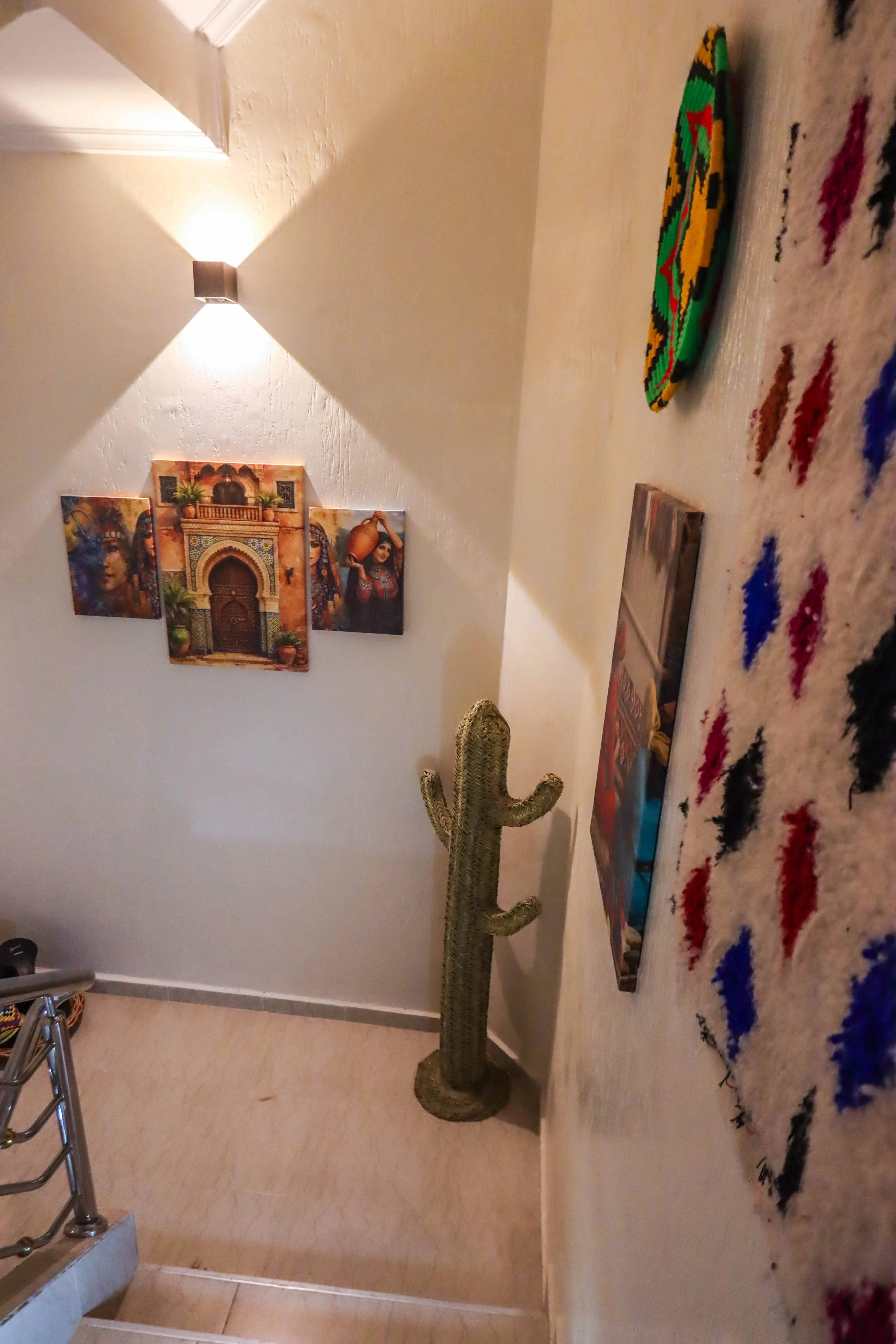 Decorated stairwell with a woven cactus sculpture and colorful wall art under warm lighting.