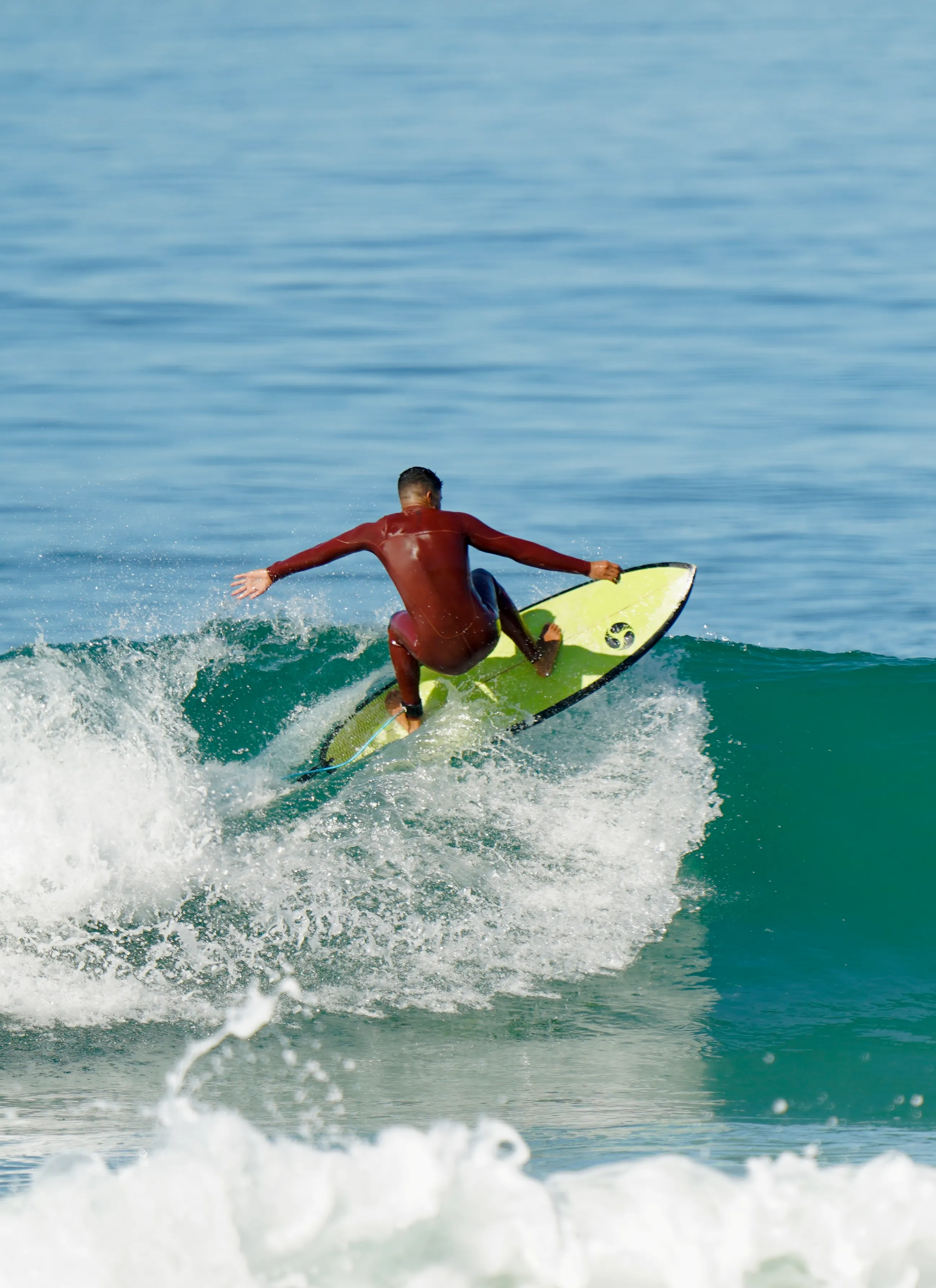 Surfer in a red wetsuit riding a green surfboard on a wave in the ocean.