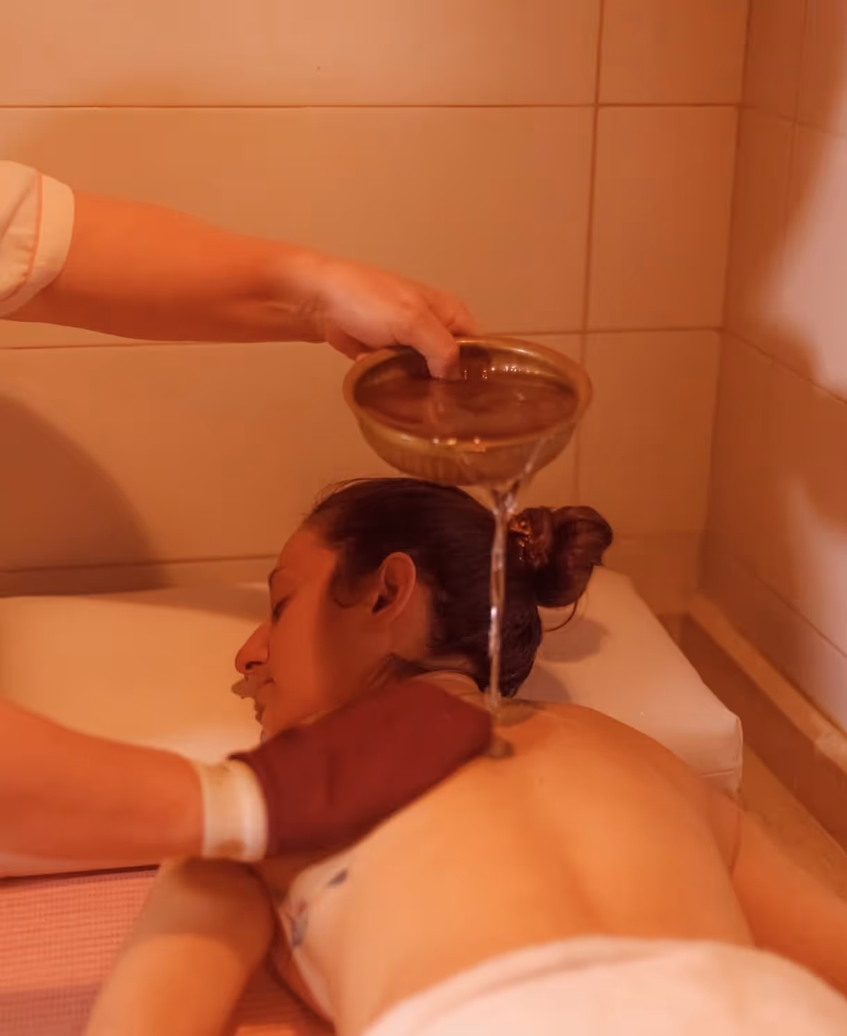 Person receiving back massage with warm water poured from a bowl in a spa setting.