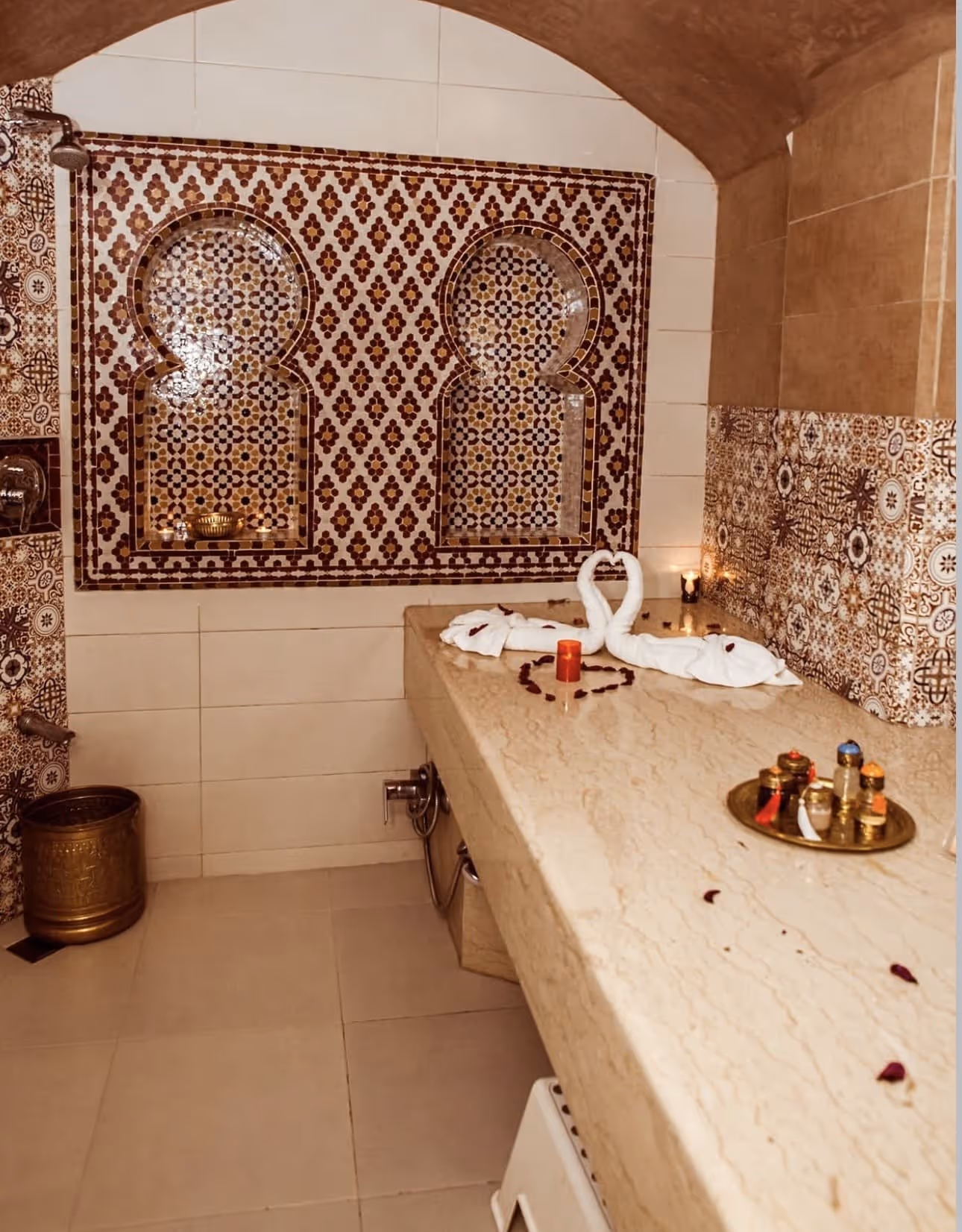 Moroccan-style spa room with patterned tiles, marble countertop, towel swans, candles, and spa oils.