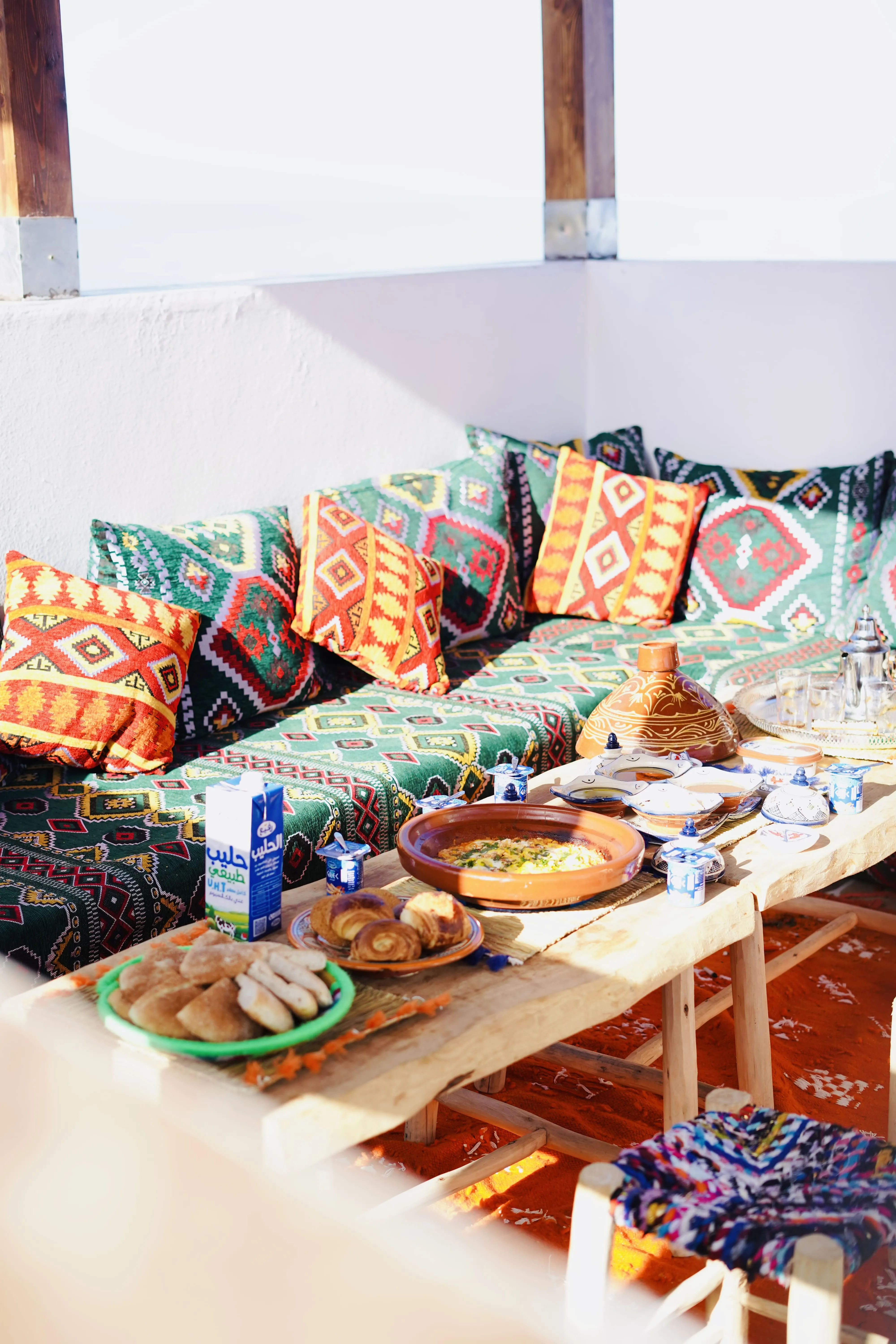 Cozy seating with colorful patterned cushions and a wooden table set with traditional dishes and bread.