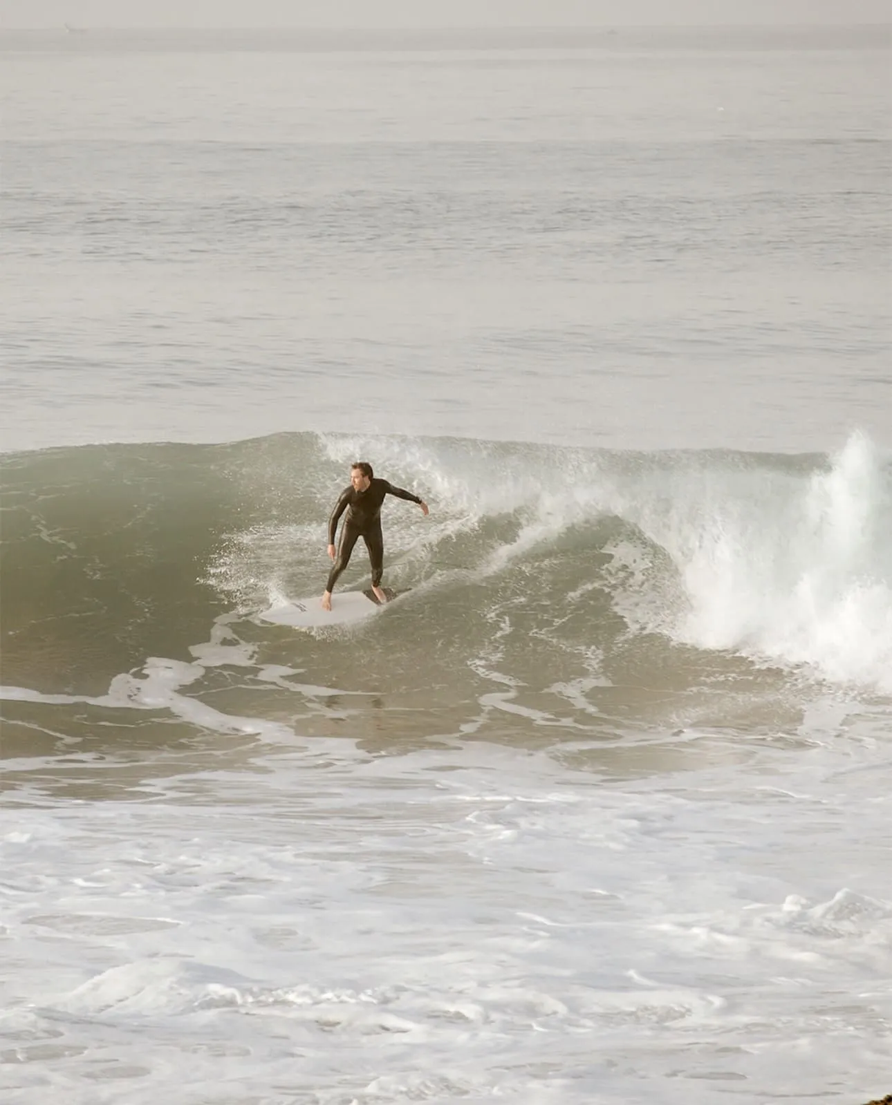 Surfer in black wetsuit riding a breaking ocean wave with white foam below.