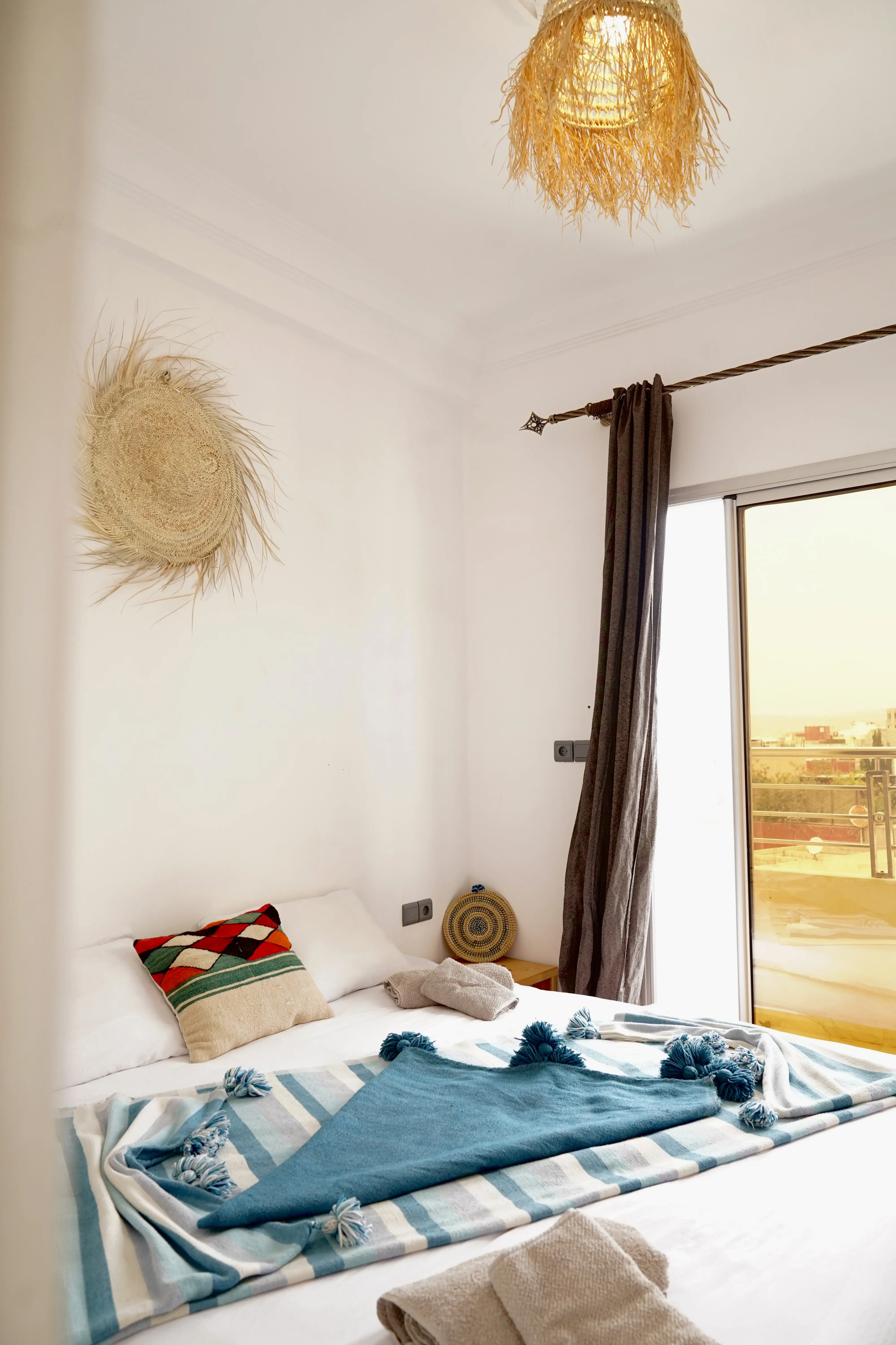 Minimalist bedroom with white walls, colorful pillow, blue throw, and sliding door with curtain.