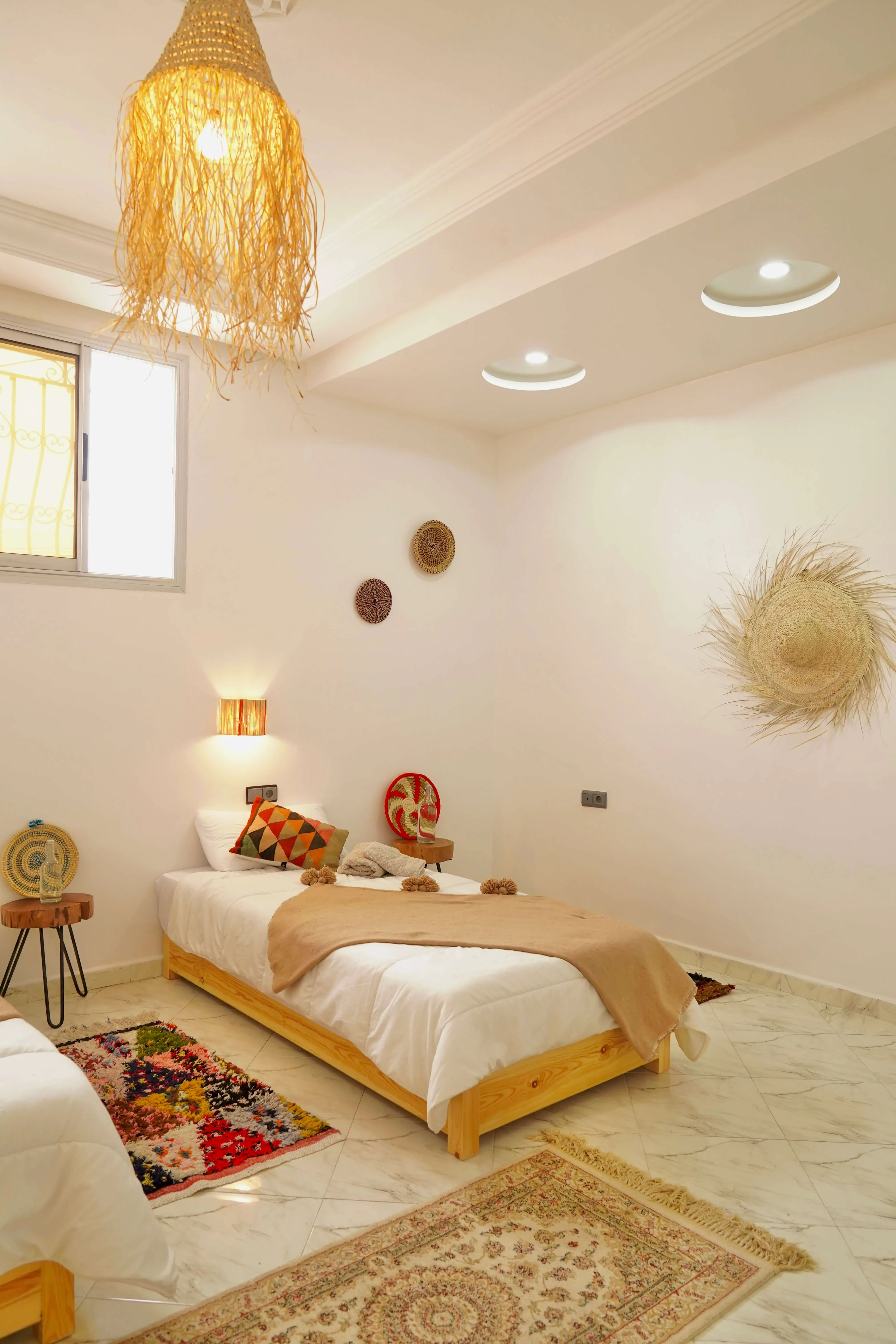 Twin beds with beige throws in a bright room with woven wall decor, rugs, and natural light.