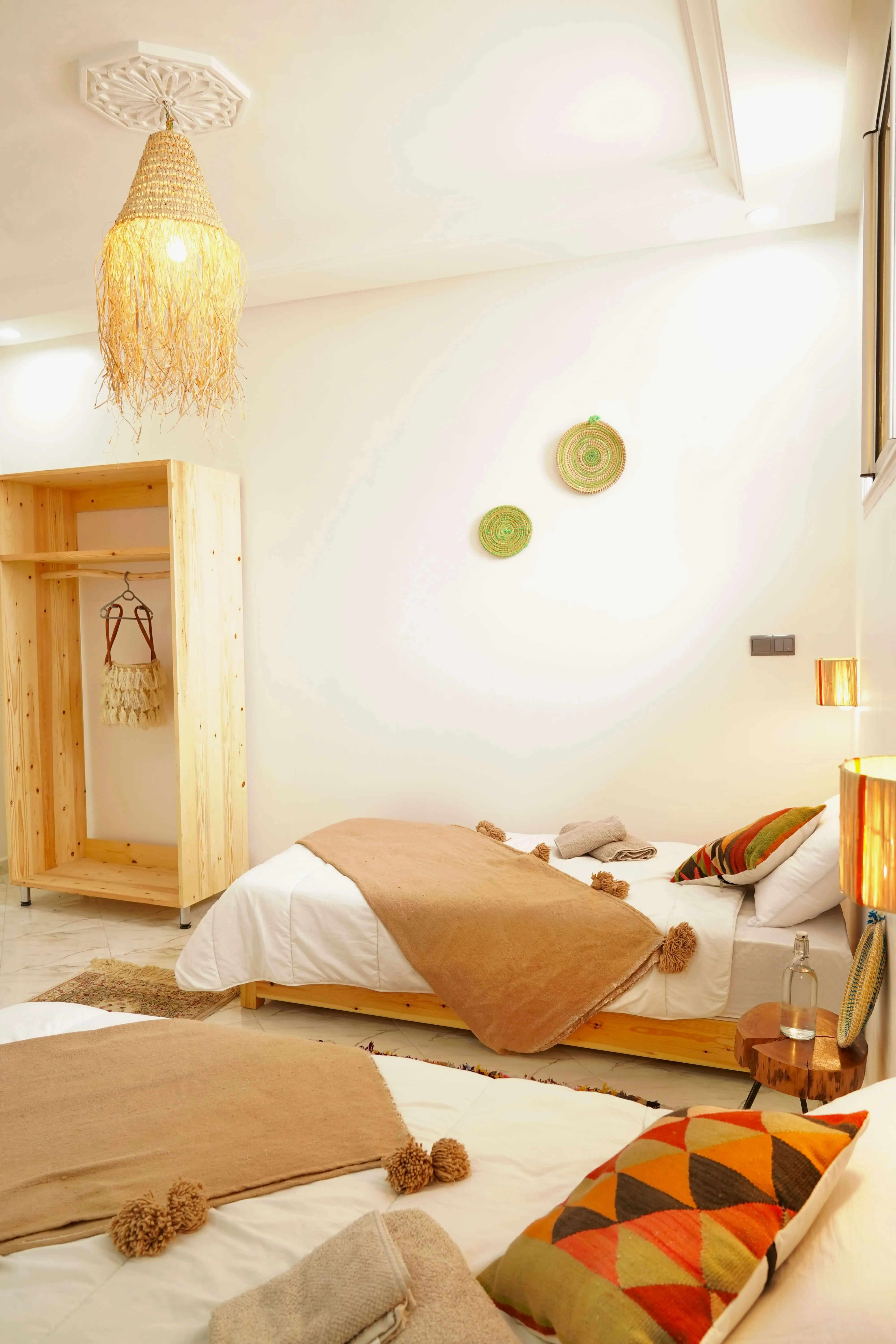 Cozy bedroom with two beds, beige throws, patterned pillows, wooden furniture, and warm lighting.