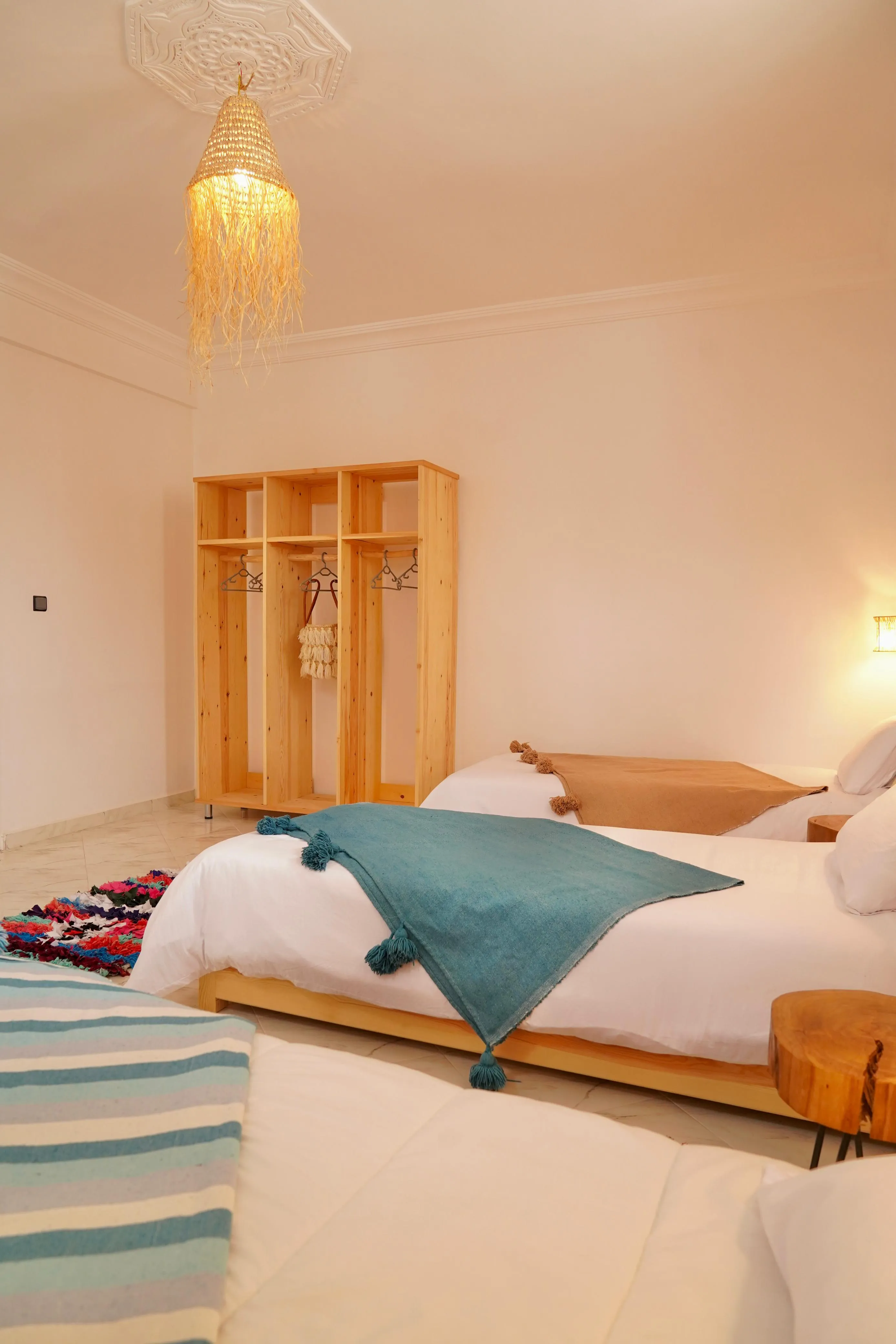 Cozy bedroom with three beds featuring colorful throws and wooden wardrobe with hangers and bag.