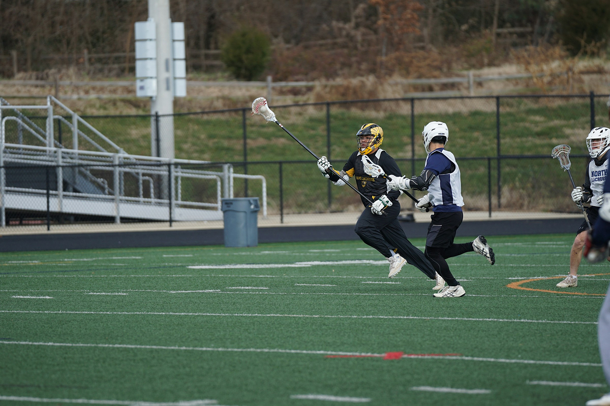 Two lacrosse players in helmets compete on a green field during a game.