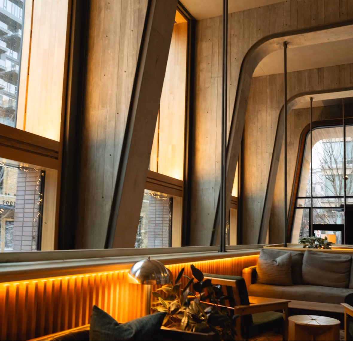 Warmly lit modern lounge interior with tall windows and concrete columns