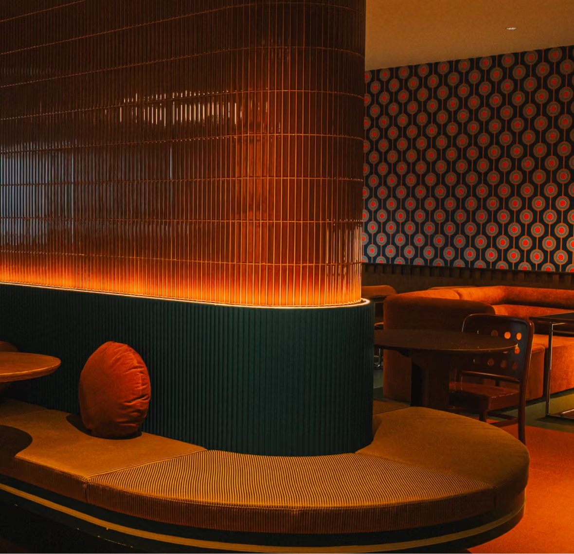 Retro lounge with glossy red tiled wall, curved banquette seating, and patterned wallpaper