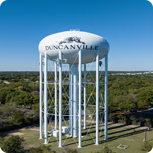 Tall white Duncanville water tower standing over green trees and clear blue sky.