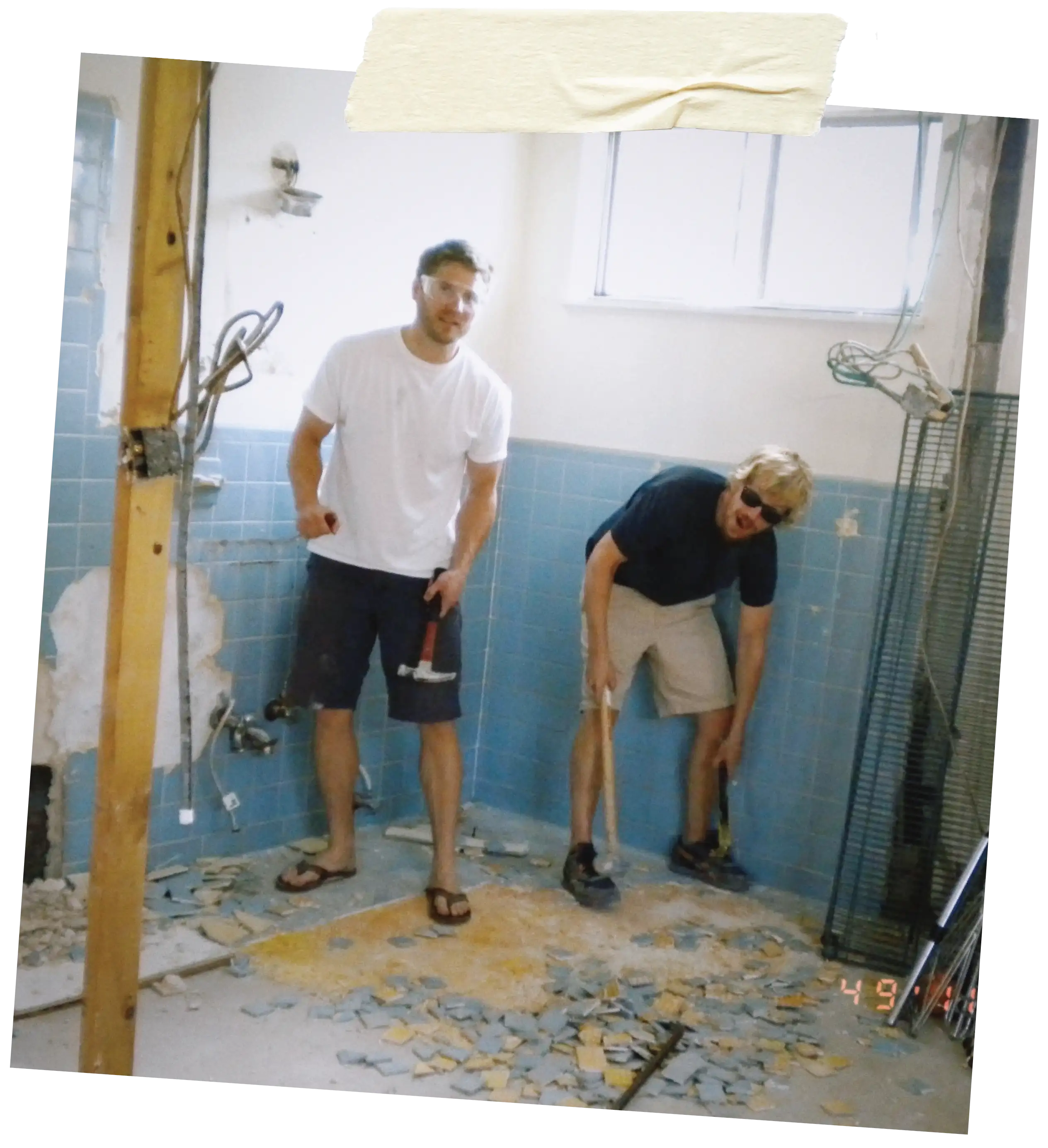 Two men breaking up blue bathroom tiles with hammers during renovation.