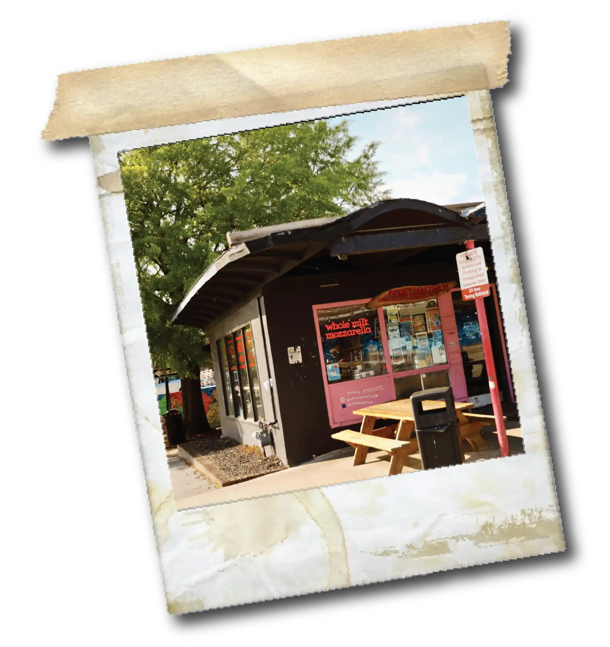 Small black building with pink window frame advertising whole milk mozzarella and picnic tables outside.