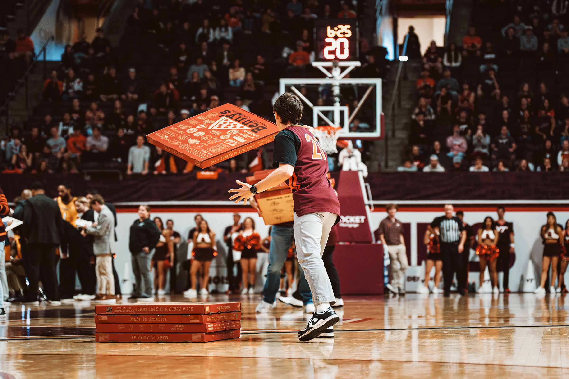 Person tossing a pizza box into the air on a basketball court during a game event.
