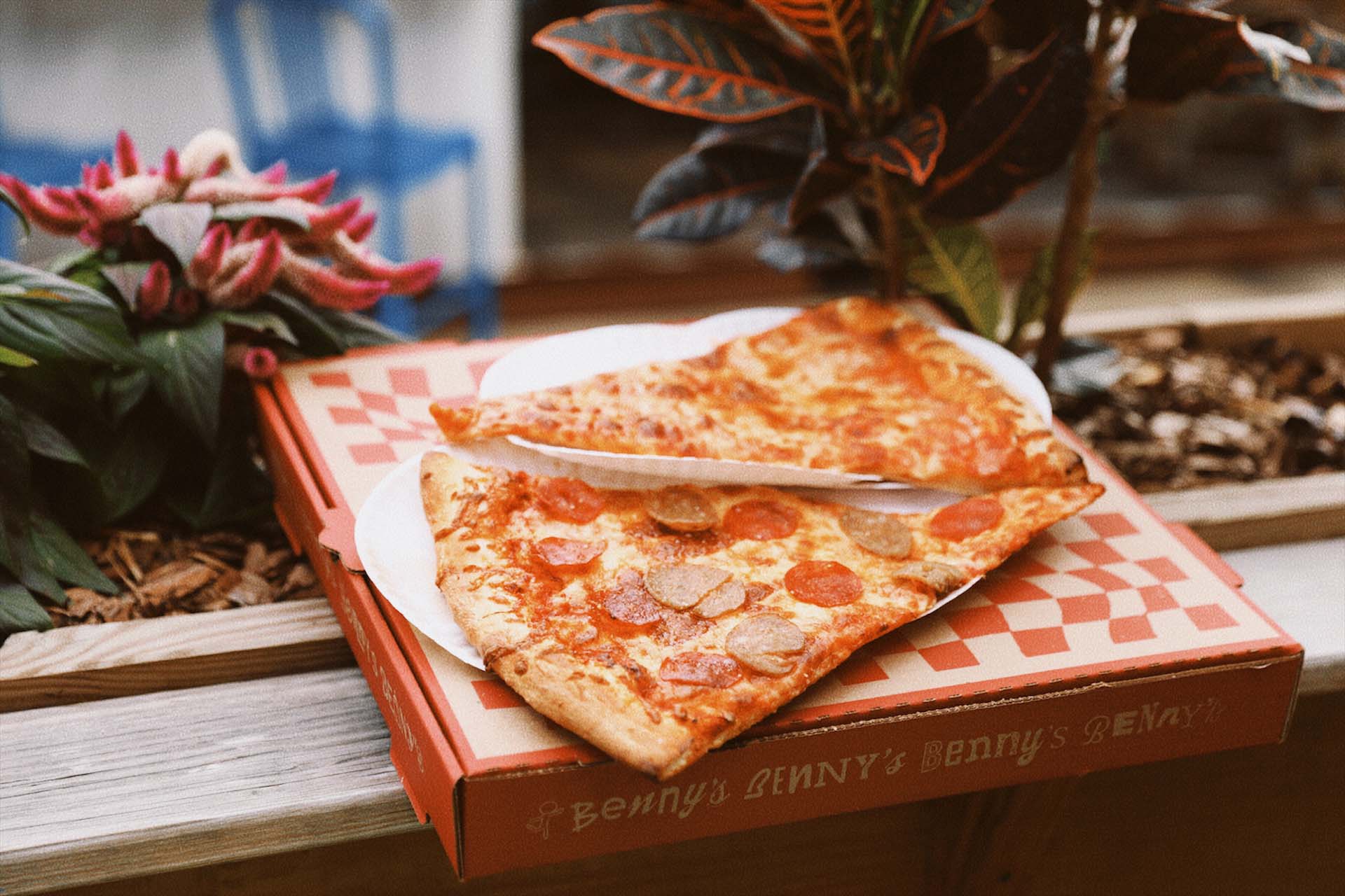 Two slices of pizza, one cheese and one pepperoni, on white paper atop a Benny's pizza box.