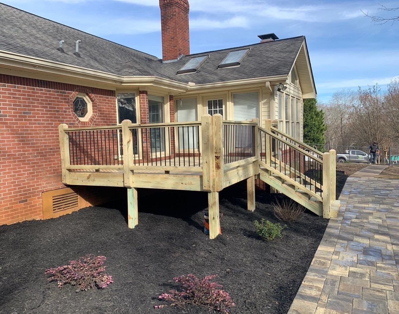 New wooden deck with metal railings attached to a brick and siding house with stairs and pathway.