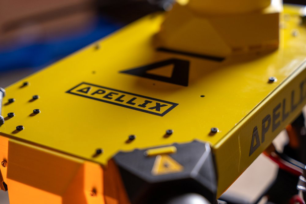 Close-up of a yellow Apellix drone showing its top surface with black screws and logo.