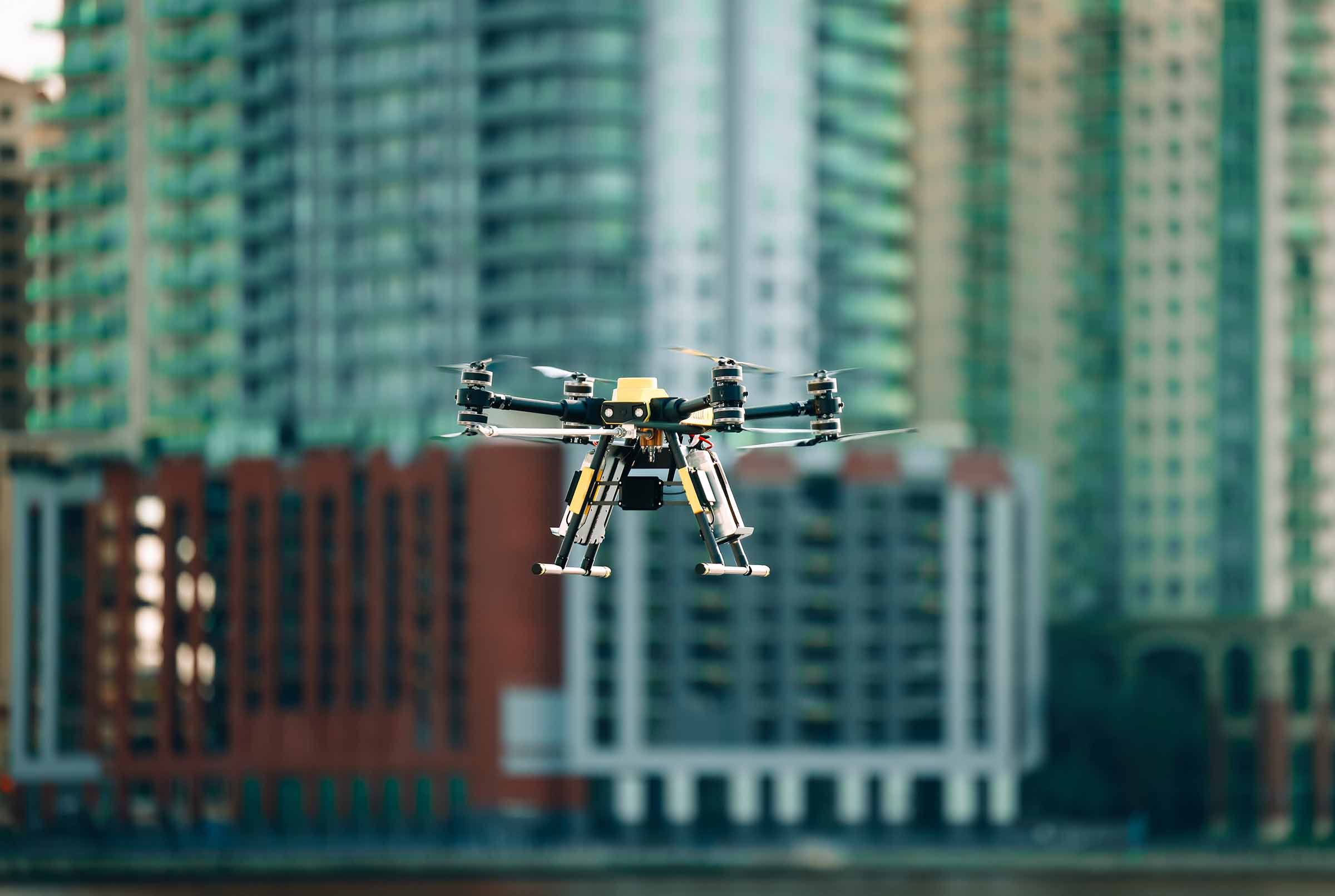 Quadcopter drone flying in front of tall city buildings.