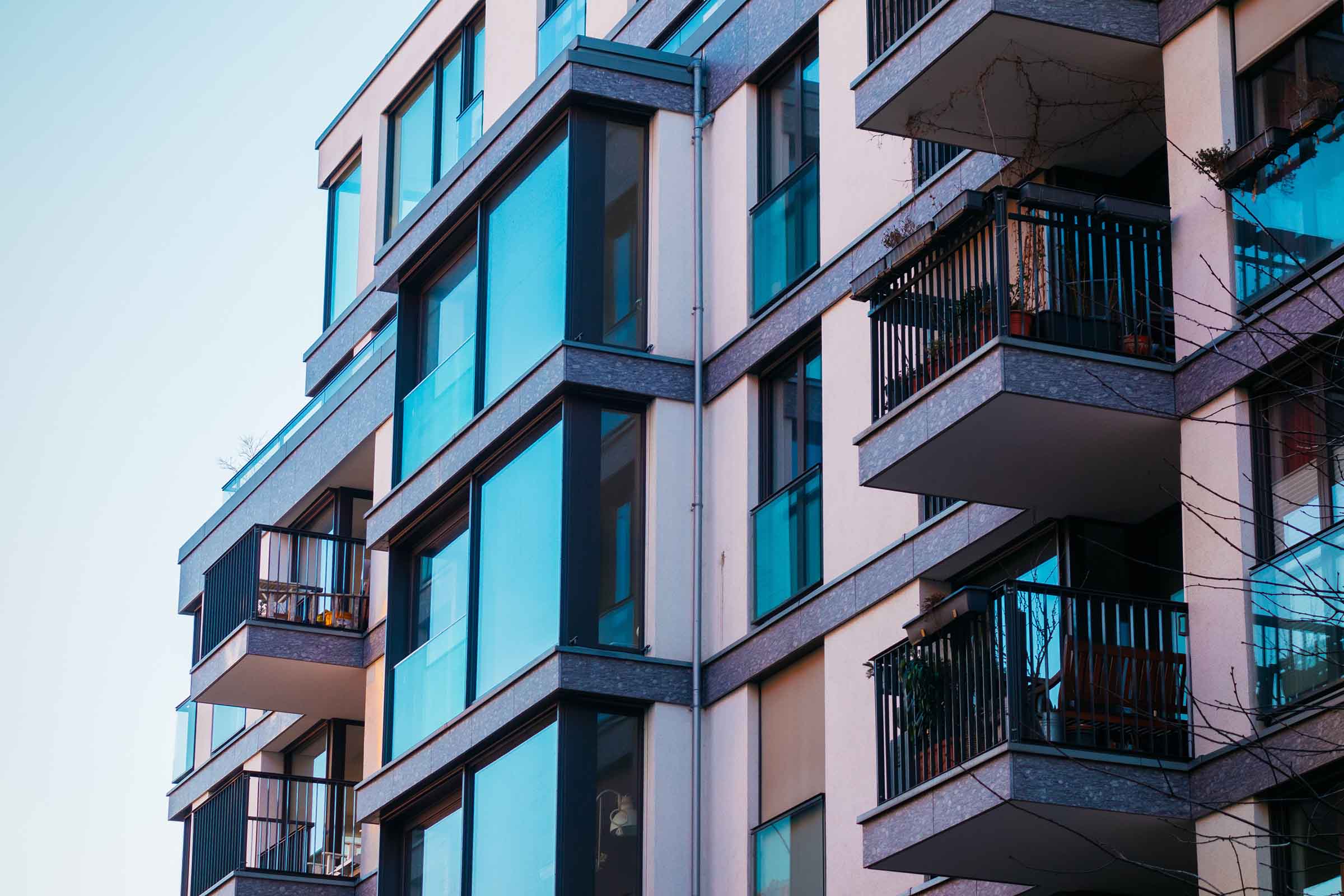 Close-up of a modern apartment building with blue-tinted glass windows and balconies with black railings.