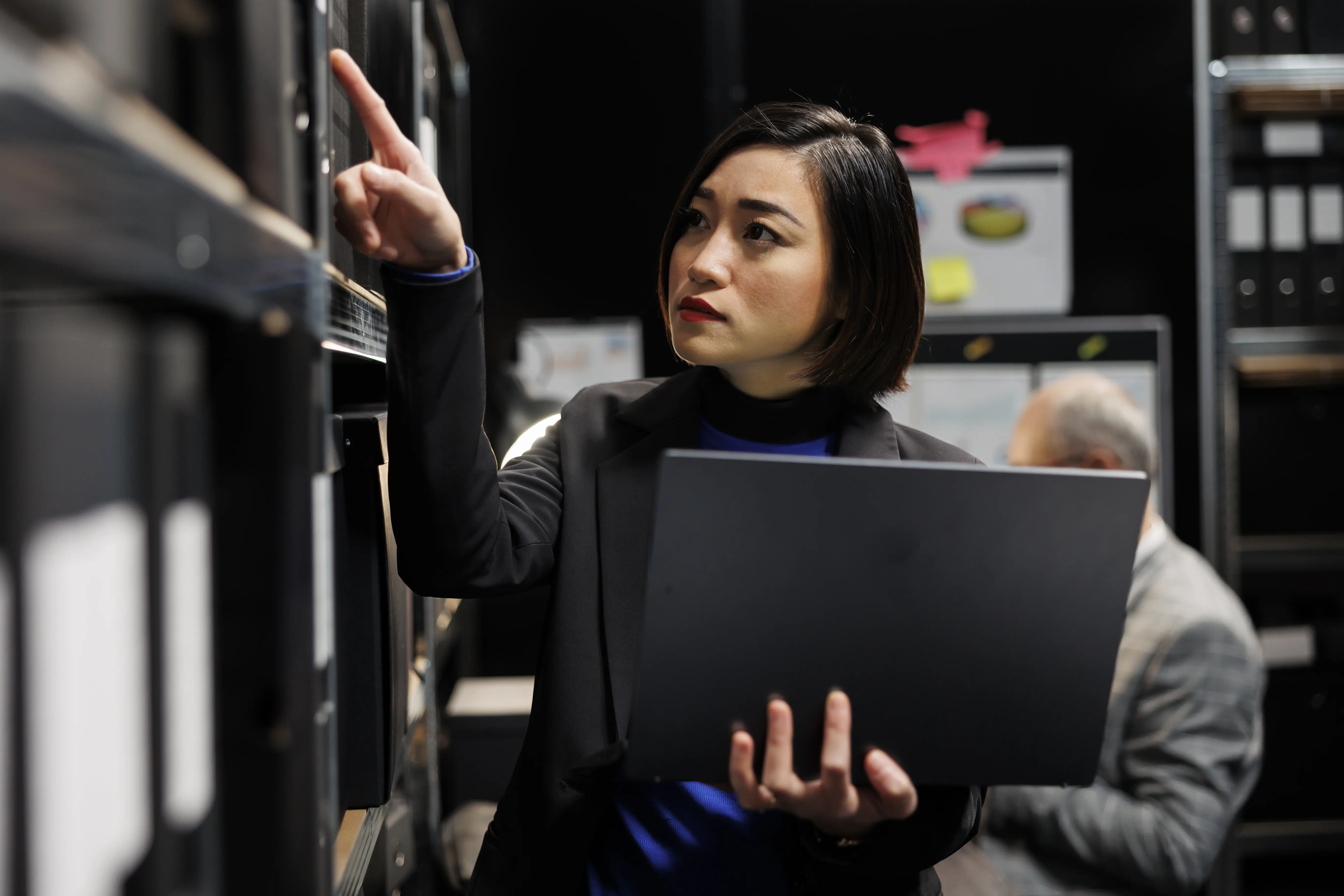Female investigator with laptop searching through case files in a dark archival records room
