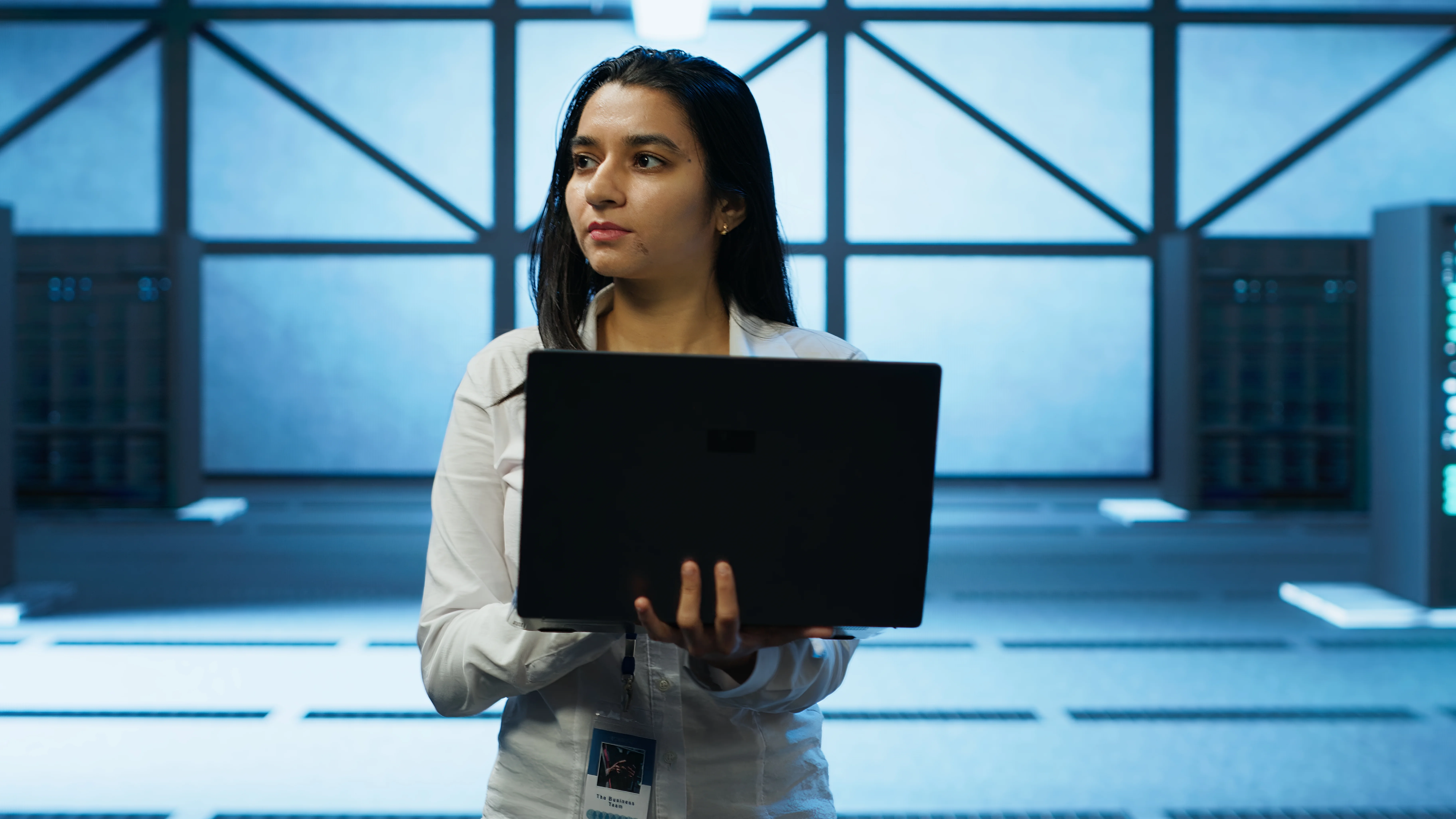 IT specialist holding a laptop while standing in a server room, with rows of servers glowing blue in the background