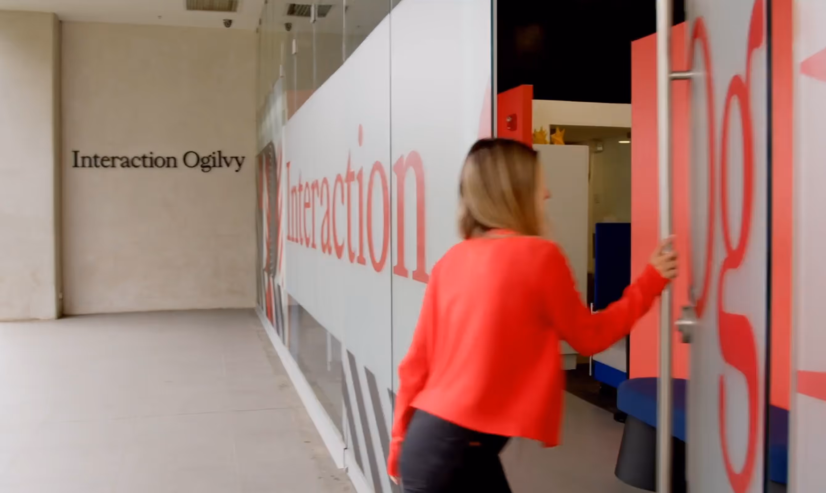 Woman in red sweater opening glass door to Interaction Ogilvy office entrance.