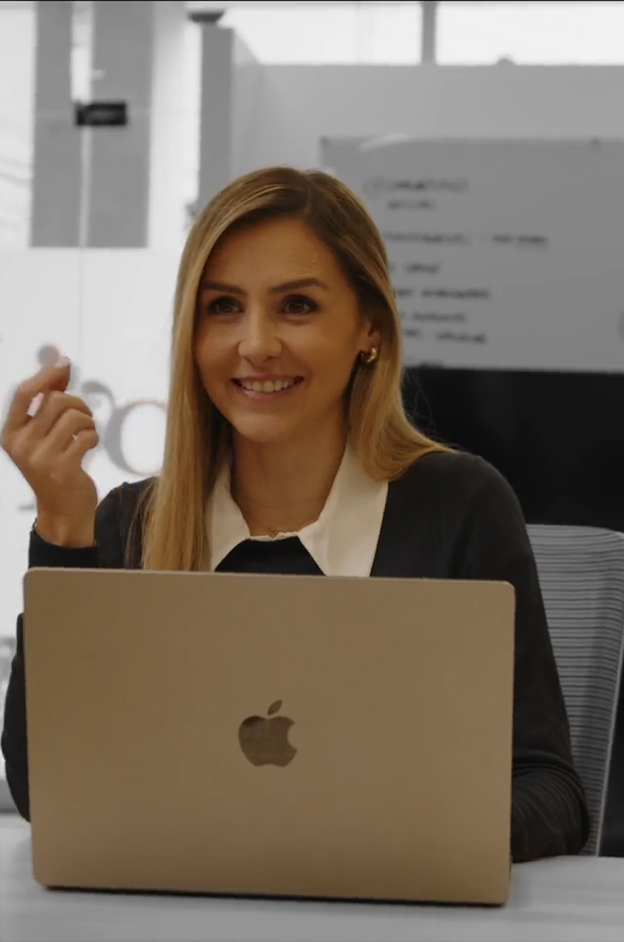 Mujer sonriendo mientras usa una computadora portátil Apple en una oficina.
