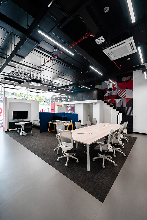 Oficina moderna con mesa de trabajo, sillas ergonómicas, y decoración geométrica roja y negra en pared.