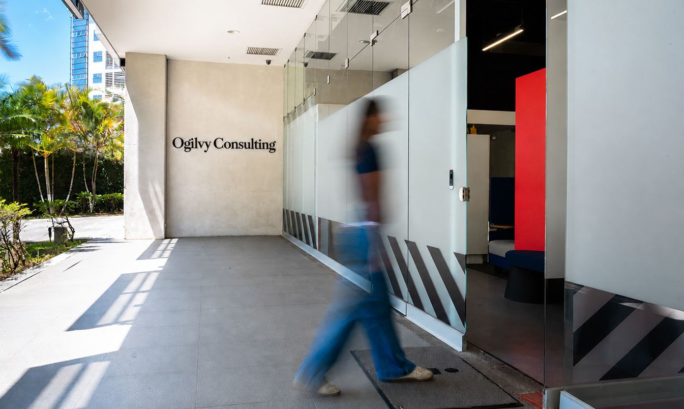 Persona borrosa caminando frente a la entrada de una oficina con el letrero Ogilvy Consulting en la pared.