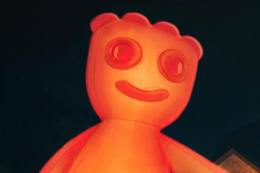 Figura inflable naranja con cara sonriente iluminada contra un fondo oscuro.