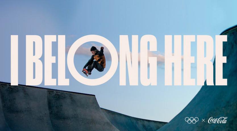 Patinador realizando un truco dentro de la letra O en la frase 'I BELONG HERE' sobre fondo azul.