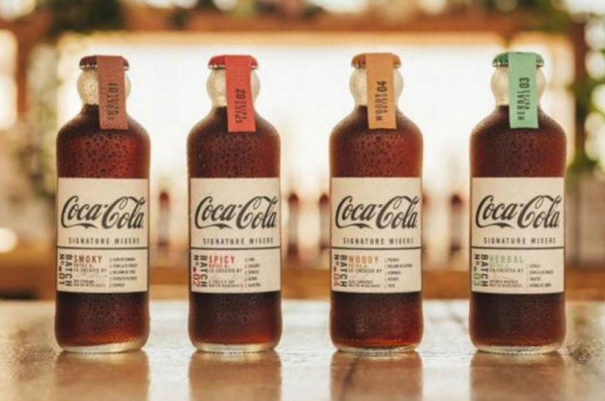 Cuatro botellas de Coca-Cola con etiquetas de mezcla exclusiva: ahumada, picante, amaderada y herbal.