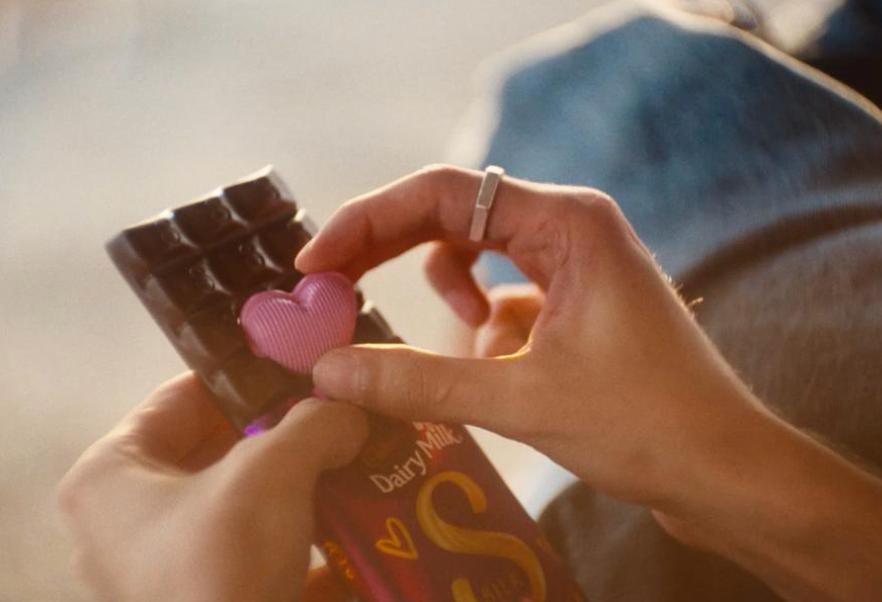 Manos sosteniendo un chocolate Dairy Milk mientras sacan un corazón rosa de la barra.