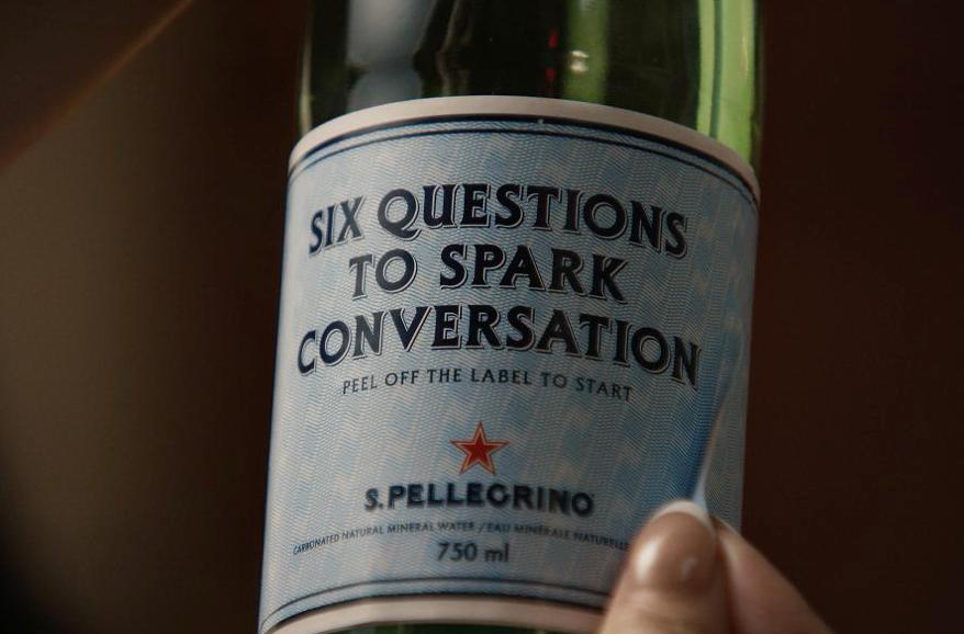 Etiqueta de botella de agua S.Pellegrino con mensaje de seis preguntas para iniciar conversación.