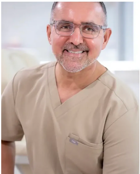 Smiling middle-aged man wearing glasses and beige medical scrubs with a pocket tag that reads Figs.