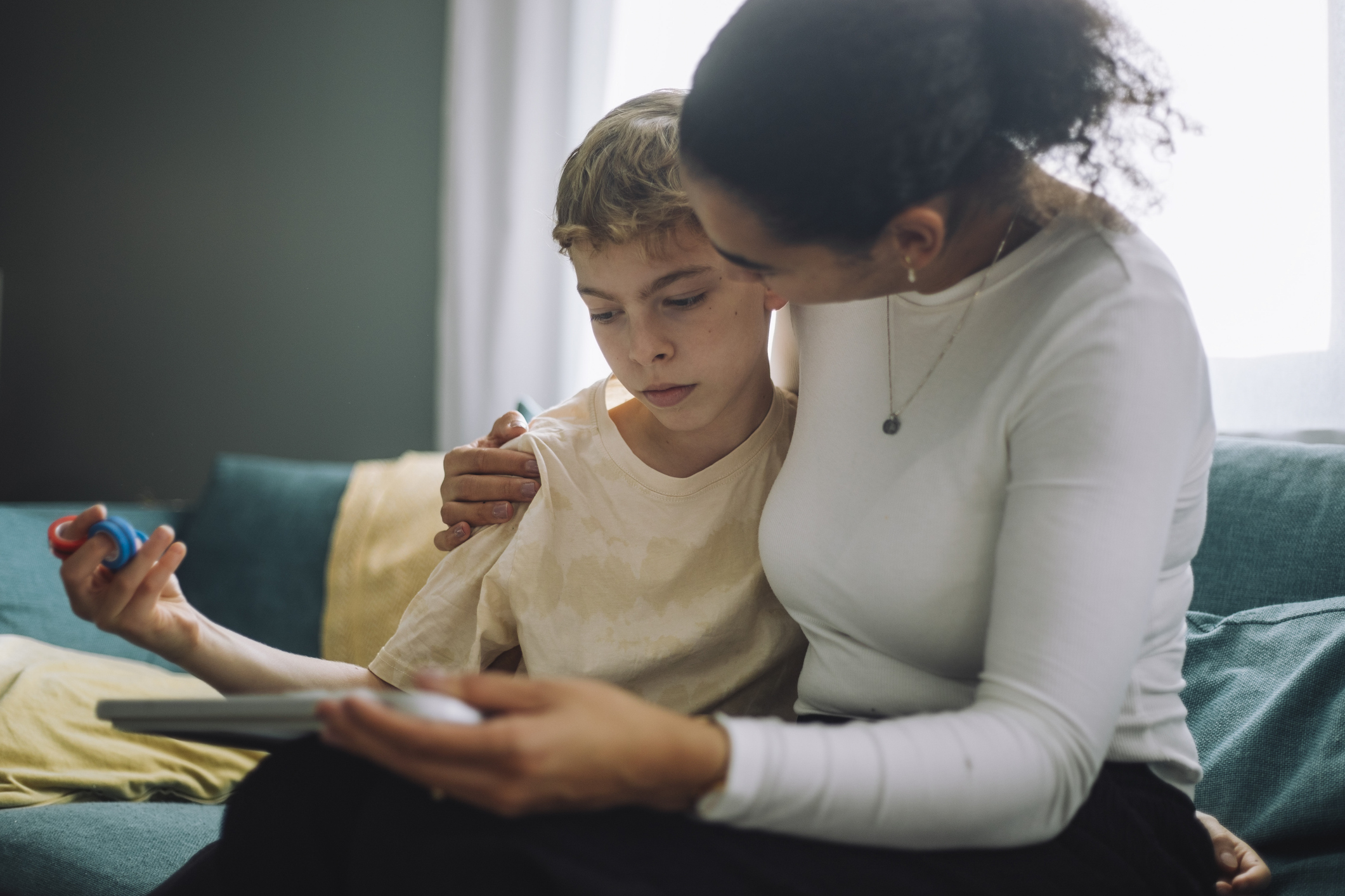 Smiling young boy with curly hair writing with a pencil at a classroom desk.