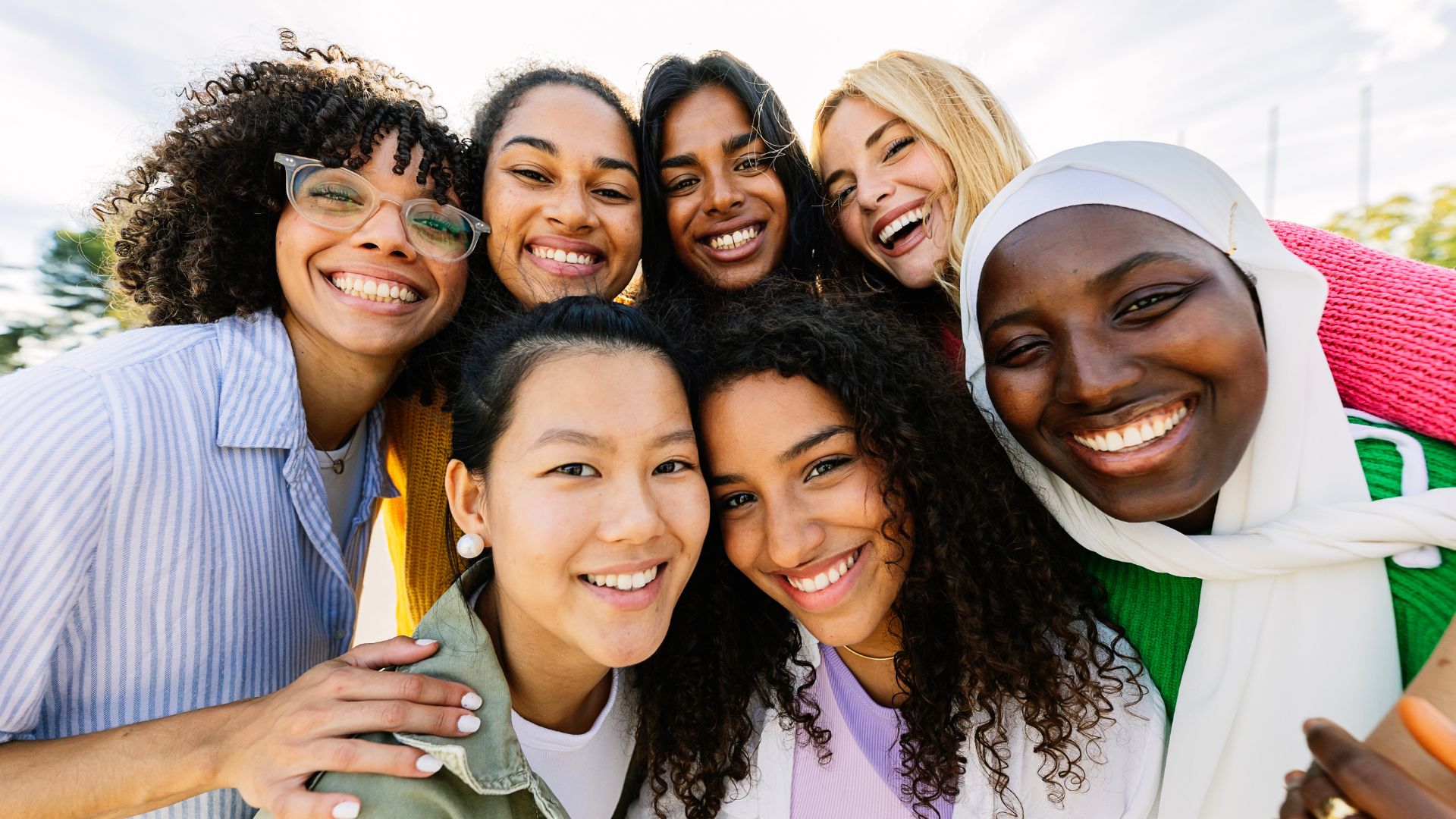 Group of happy diverse young women smiling closely together outdoors on a sunny day.