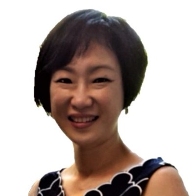 Smiling woman with short black hair wearing a black and white patterned sleeveless top.