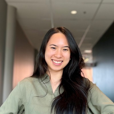 Smiling woman with long dark hair wearing a green shirt standing indoors in front of a hallway.