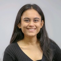 Smiling young woman with long black hair wearing a black top against a gray background.