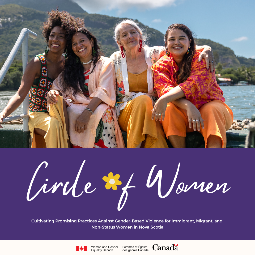 Four diverse women smiling and sitting closely outdoors with water and mountains behind them.