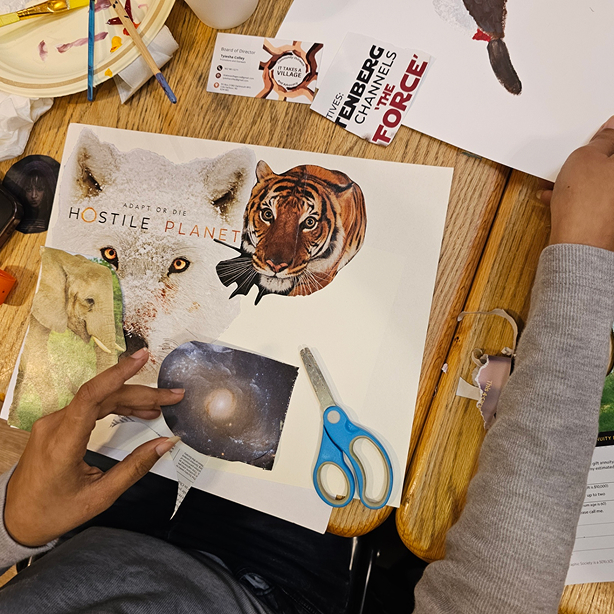 Person creating a collage with animal images, galaxy, scissors, and business cards on a wooden table.