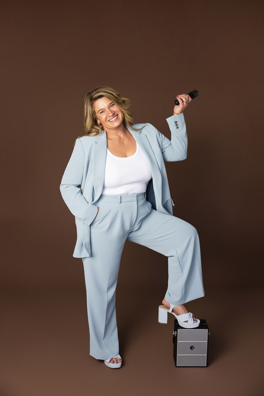 Tamiko McGurk smiling while holding a microphone against a warm brown studio backdrop