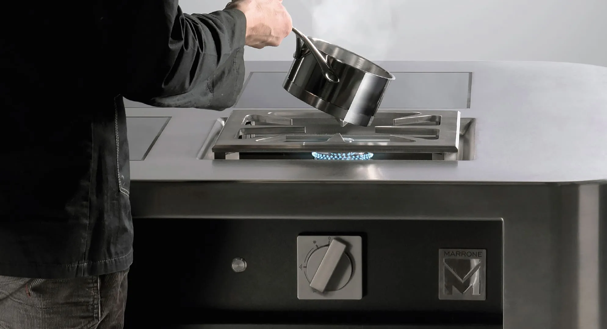 Person holding a steaming stainless steel pot above a lit gas burner on a modern stovetop.