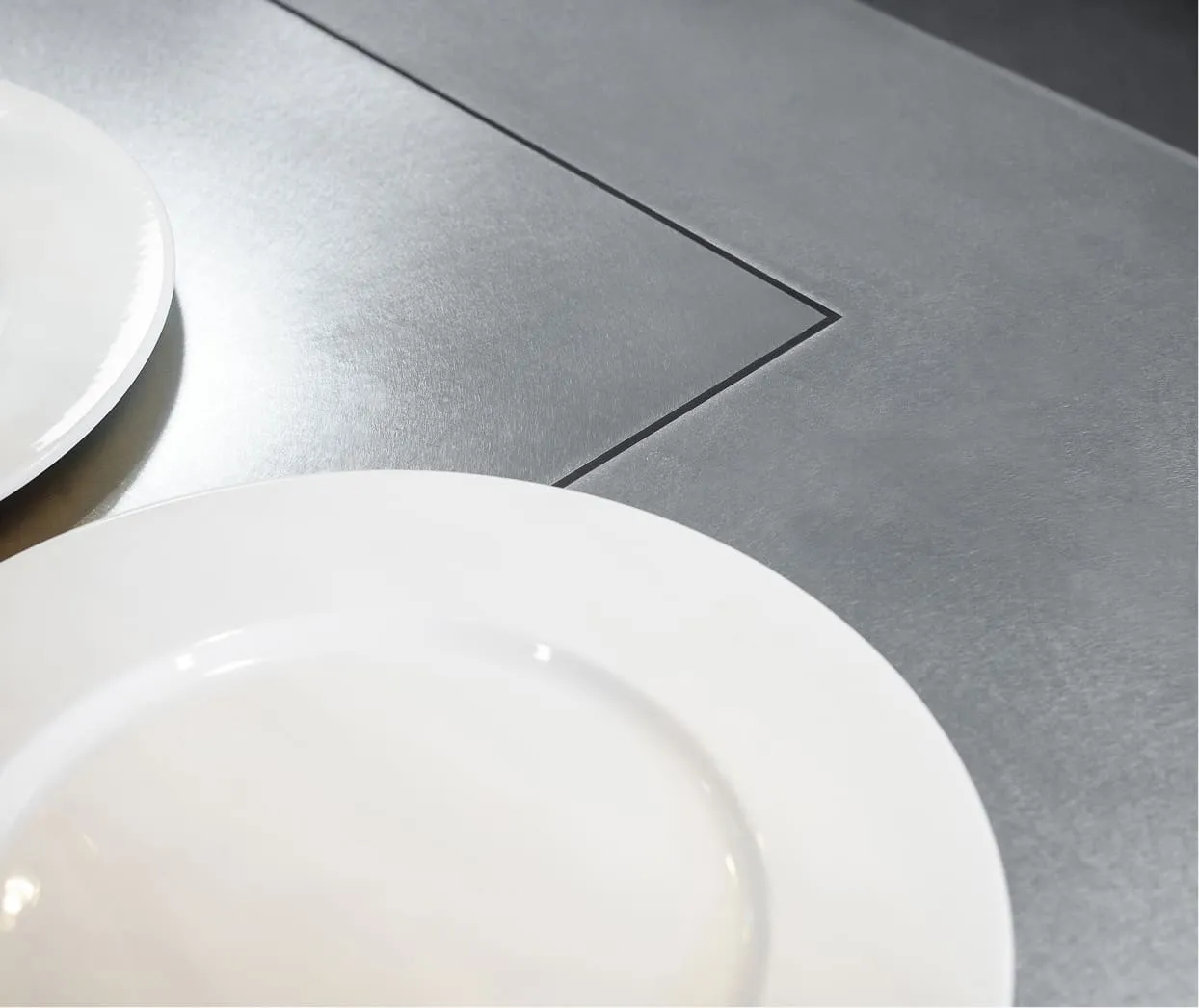 Two empty white plates placed on a metallic gray table with a recessed rectangular design.