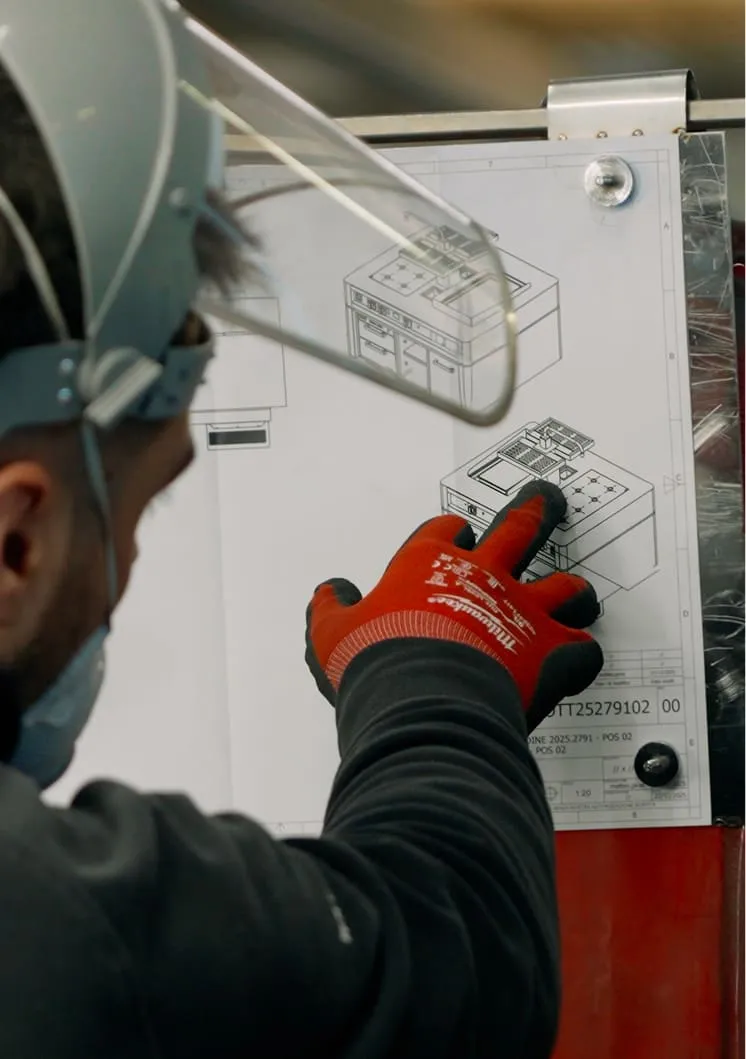Person wearing safety gear and orange gloves pointing at a technical drawing of a machine on a clipboard.