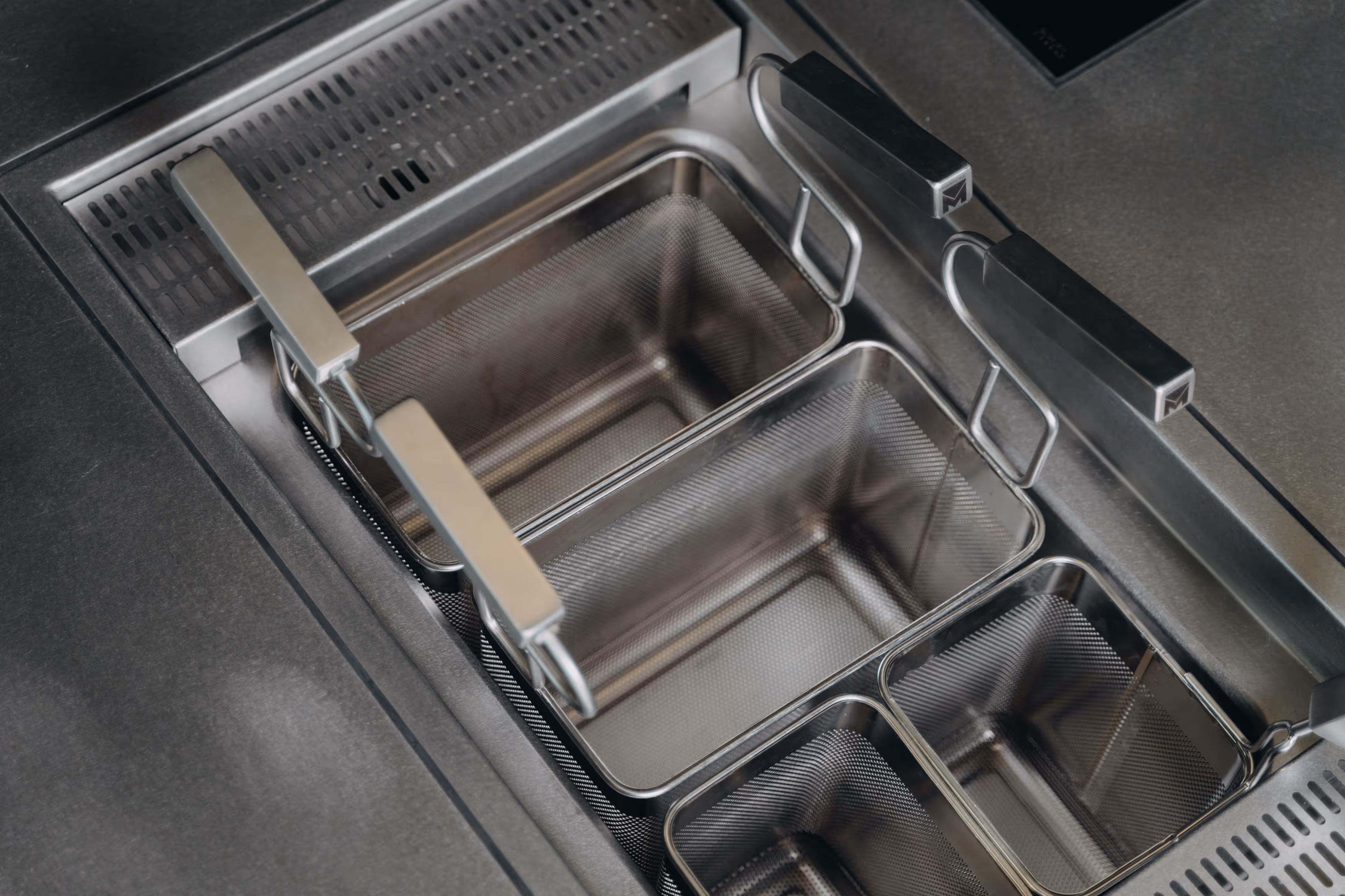 Close-up of empty stainless steel deep fryer baskets with handles inside a commercial fryer unit.