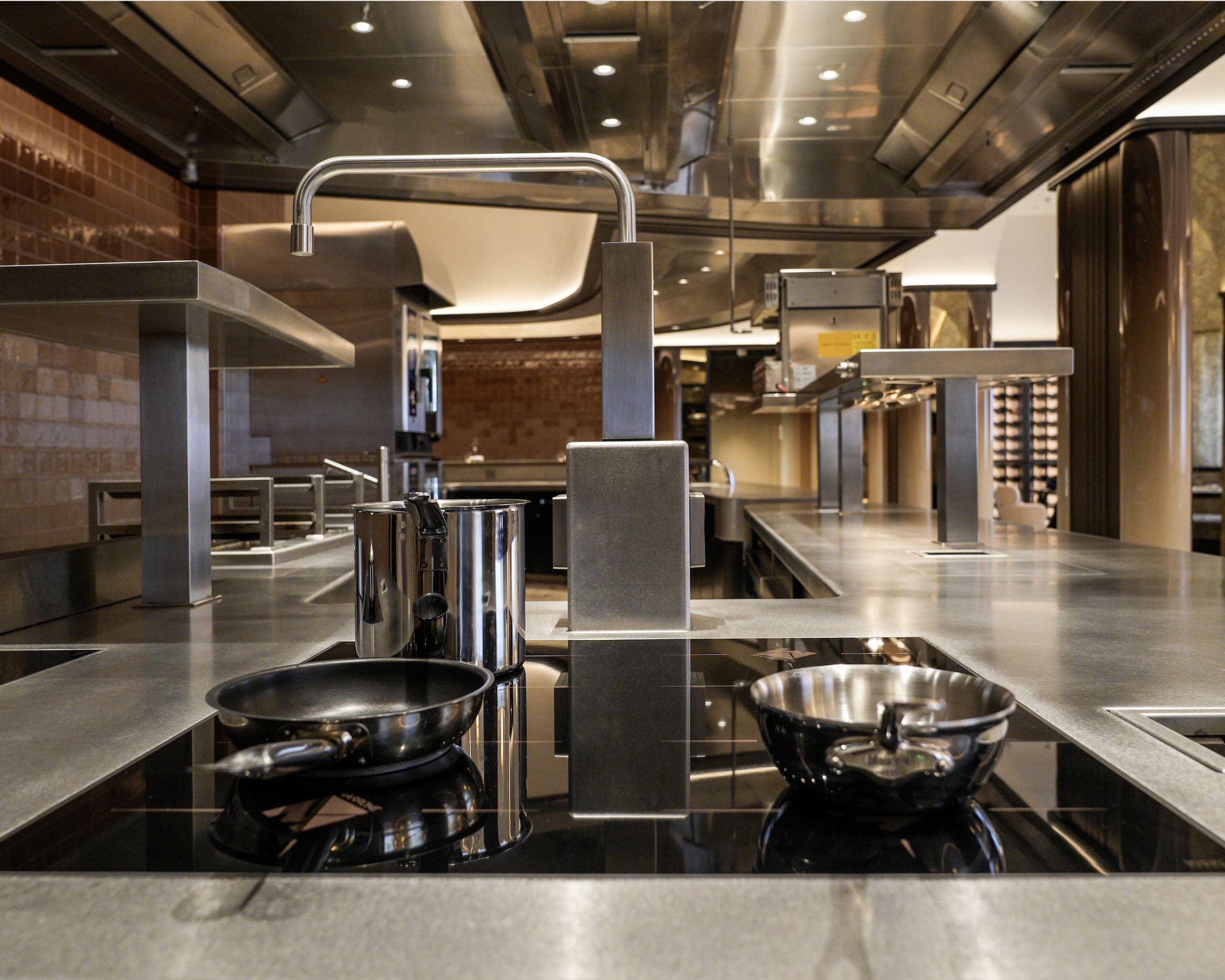 Modern professional kitchen with stainless steel countertops, a faucet, a frying pan, and a saucepan on an induction cooktop.