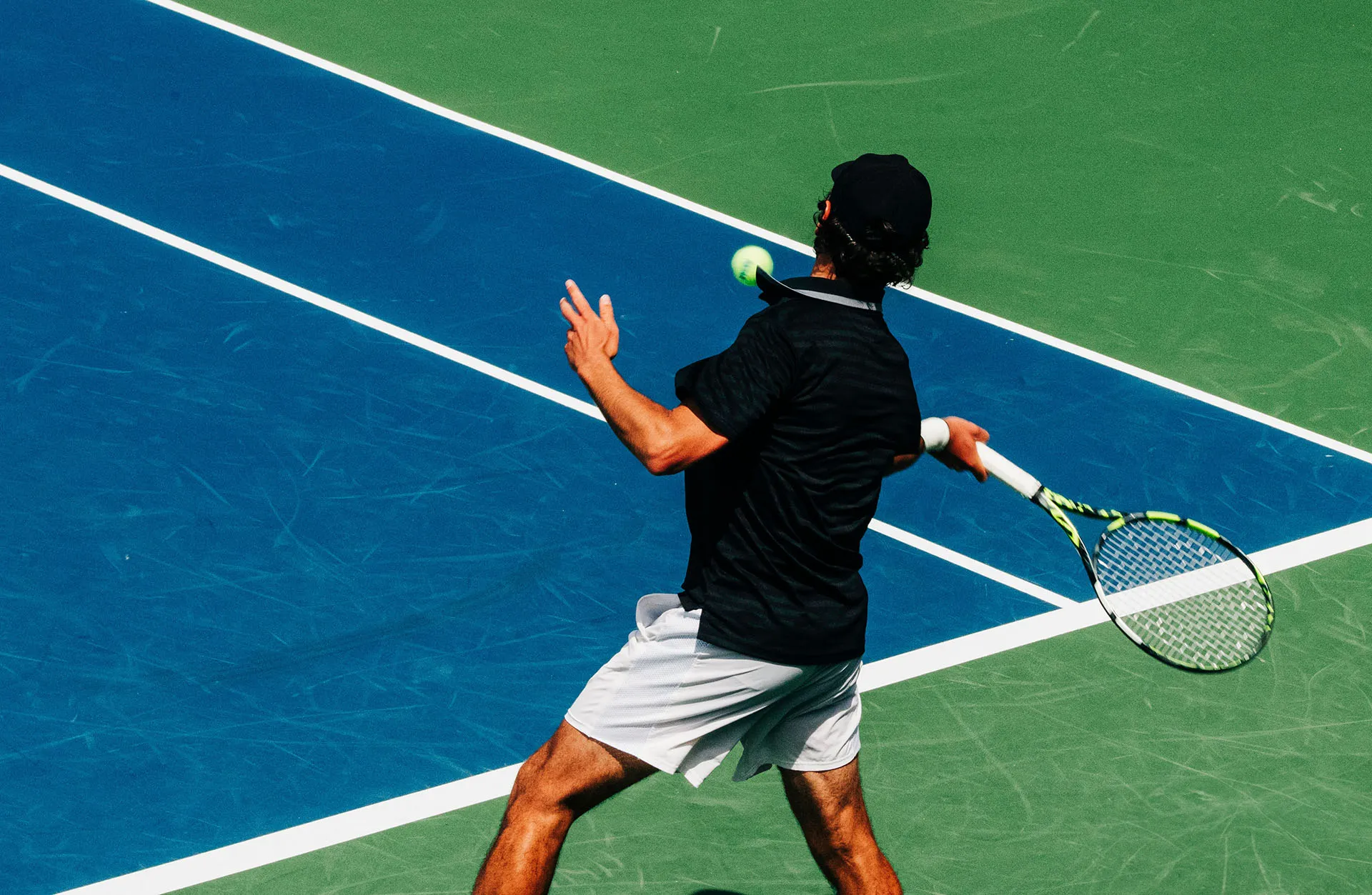 Tennis player in black shirt and white shorts hitting a forehand shot on a blue and green court.